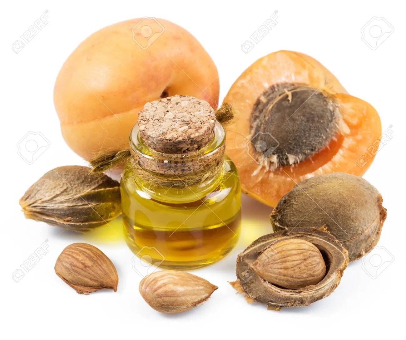 A small glass bottle of aruna kullu handloom GUTTI KA TEL (Apricot oil) with a cork, surrounded by whole apricots, pits, and kernels on a white background.