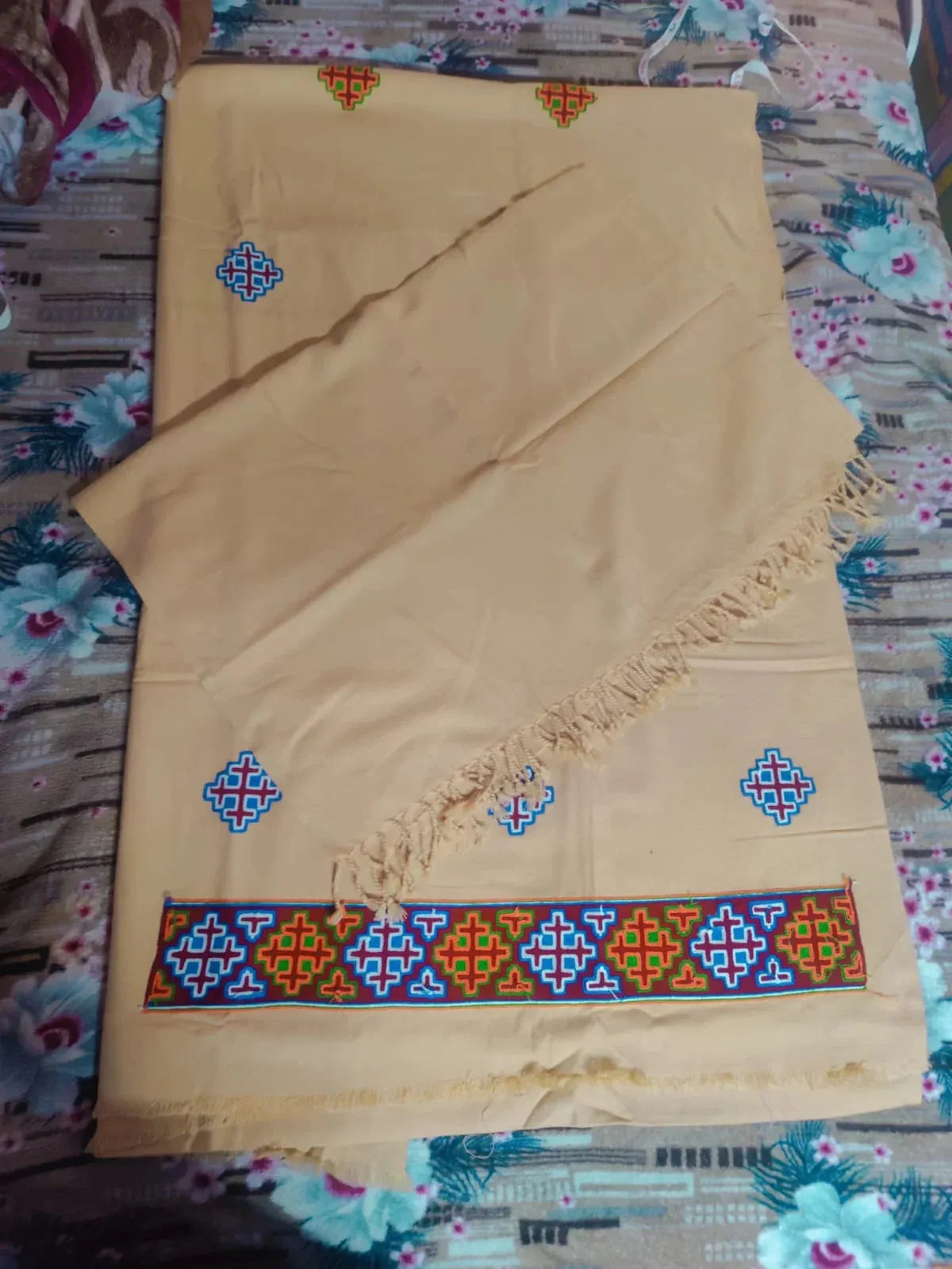 A cream woolen handloom suit by aruna kullu handloom, featuring colorful geometric embroidery and a kullu patti border, is neatly folded with a fringed edge. This 4-meter suit comes with a stole, reflecting classic kullu designs.