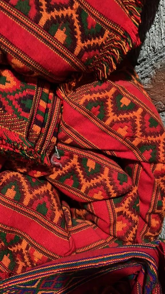 Close-up of aruna kullu handloom's KULLU Patti (LACE) Border for Suits, Kurtis, and Dress Material (3 M), showcasing vibrant red, green, orange, and black geometric patterns with traditional kullu border on a textured stone background.