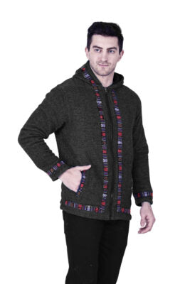 A man stands with one hand in his pocket, wearing the aruna kullu handloom Woolen Winter Wear ZIPPER HOODIE Jacket for MEN in grey, featuring colorful patterned trim on the zipper, cuffs, and hem against a white background.