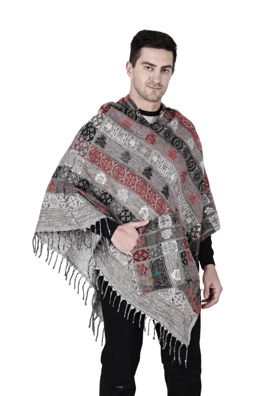 A man with short dark hair and a slight smile stands against a white background wearing the aruna kullu handloom kullu shawl woolen poncho with hood for men in grey, featuring red, black, and gray designs and fringed edges.