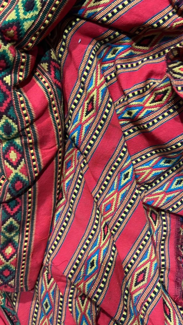 A close-up of aruna kullu handloom's vibrant red KULLU Patti (LACE) Border (3 M) for suits, kurtis, and dress material, featuring intricate geometric patterns in yellow, blue, green, and black with a traditional diamond and stripe design.