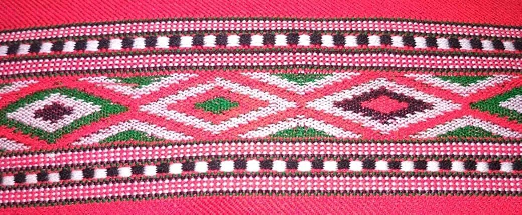 A close-up of aruna kullu handloom KULLU Patti (LACE) Border for Suits, Kurtis, and Dress Material (3 M), showcasing colorful woolen geometric patterns with diamond shapes and striped borders on a vibrant pink background.
