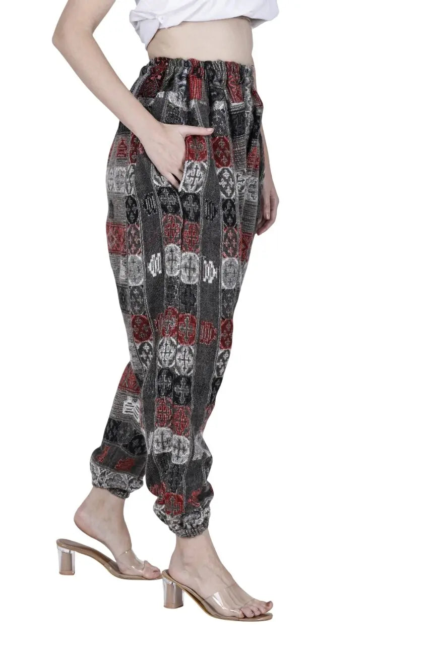 A person models aruna kullu handloom's Wool Super Soft Warm Pyjamas WITH KULLU PATTI WORK, featuring red, black, and white geometric designs, paired with a white crop top and clear heels, standing sideways with a hand in the pocket.