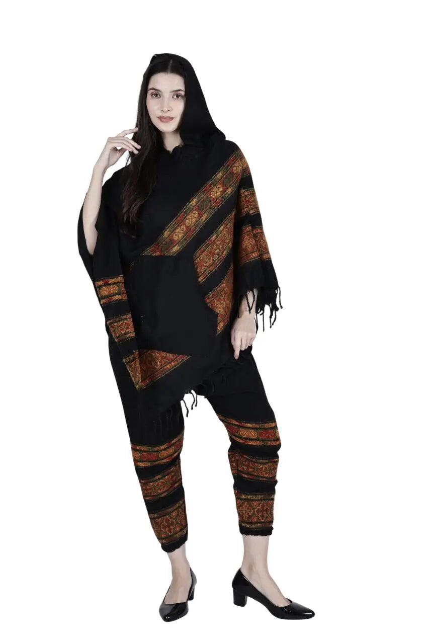 A woman models the aruna kullu handloom kullu shawl combo poncho and pajama black 3 patti, featuring traditional patterns. She stands against a white background, wearing black heels and has long hair with one hand near her face.
