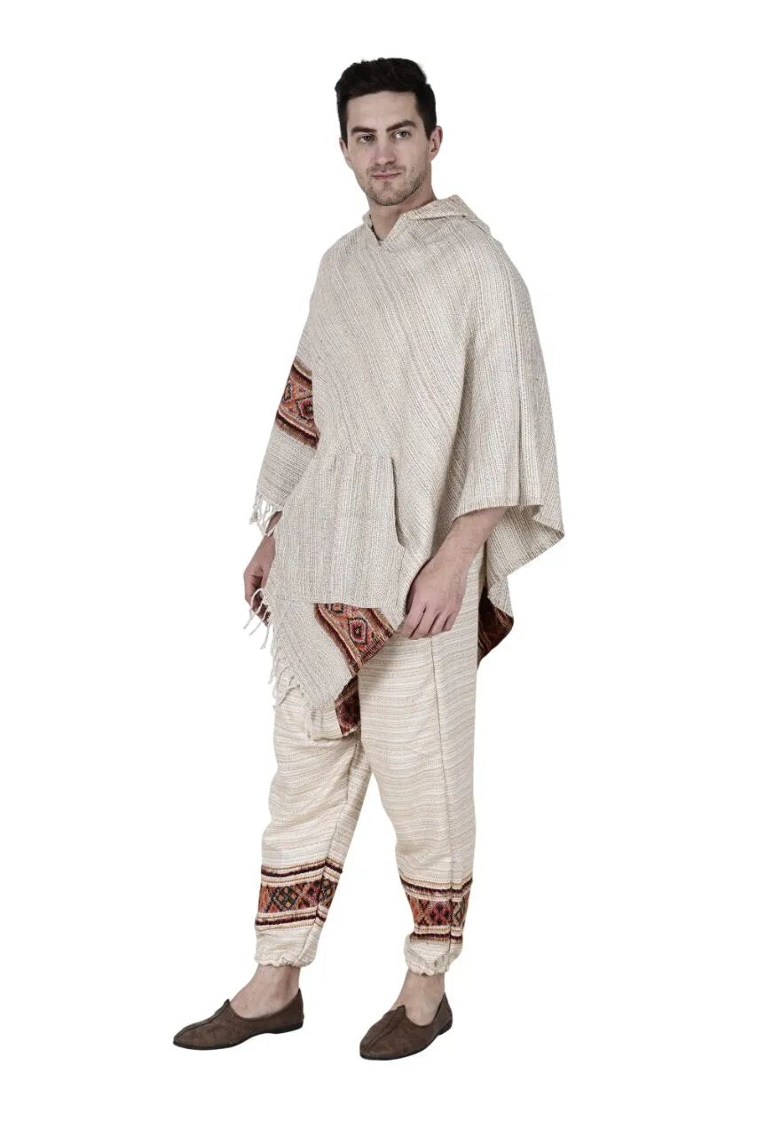 A man wears the Combo pajama and poncho white singal patti from aruna kullu handloom, featuring handwoven multicolored edge embroidery. He looks to the side and pairs the set with brown slip-on shoes.