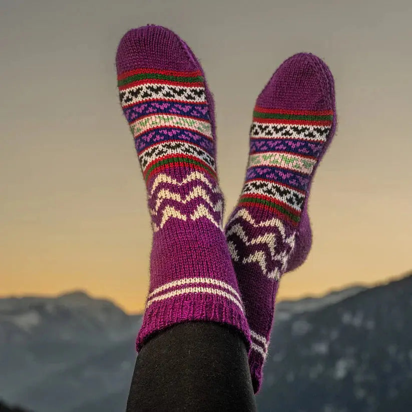 A person relaxes with their feet up, wearing aruna kullu handloom Woollen Traditional Hand Made Kullu Socks (Multicolour, Free Size), set against snowy mountains and a glowing sunset sky.