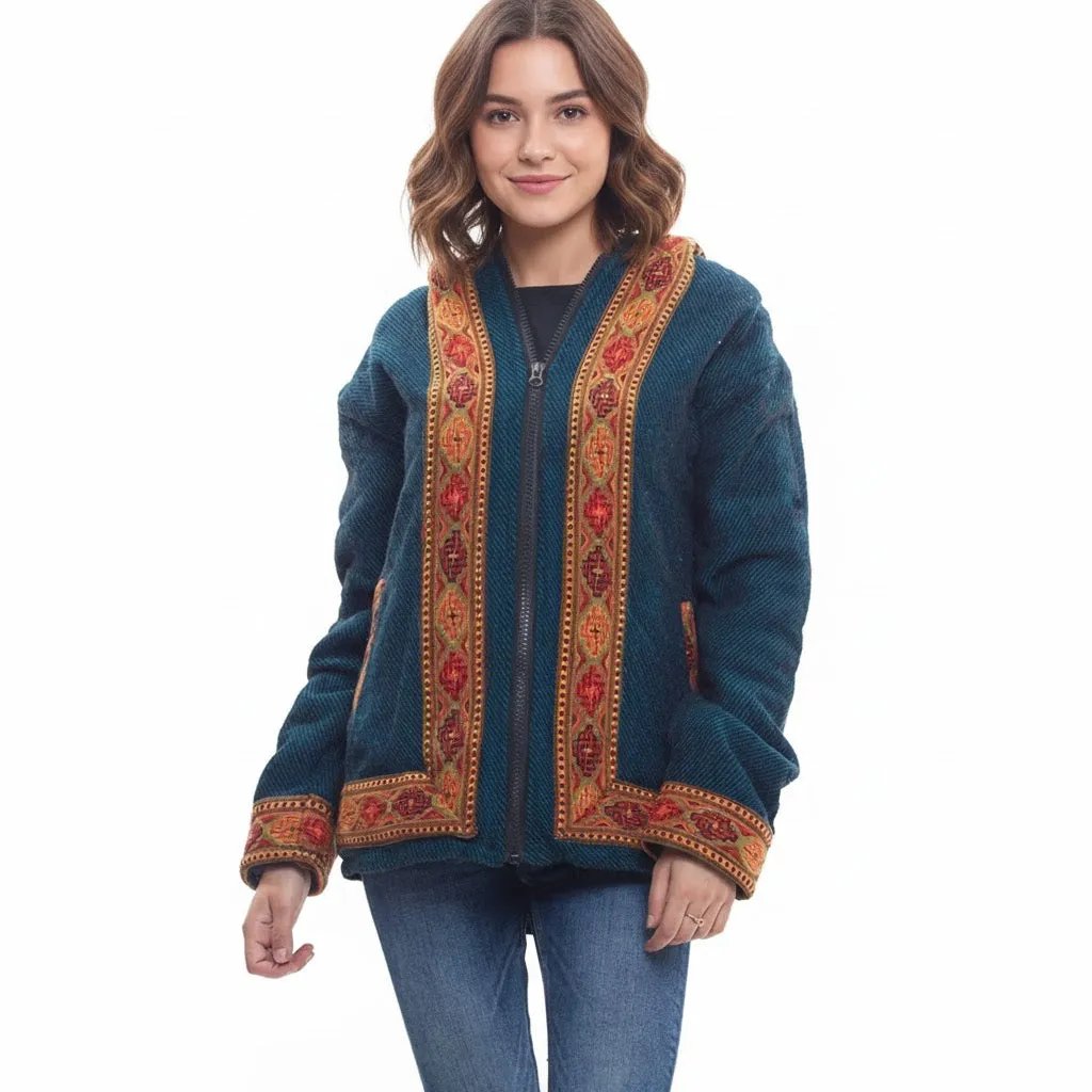 A woman with wavy brown hair smiles in front of a white background, wearing the aruna kullu handloom Himachal handicrafts woolen winter wear zipper hoodie jacket for men & women with Kullu Patti work in blue.himachal products online himachali products online bhuttico online shopping himachal handloom online himachal products online shopping