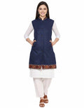 A woman smiles, posing in an aruna kullu handloom "Check navy blue long jacket with kullu lace work" over a white kurta and pants. She wears brown sandals and keeps her hands in the jacket's pockets against a white background.half jacket for women khadi half jacket for ladies ladies half jacket cotton women's half jacket ladies sadri design winter half jacket for women